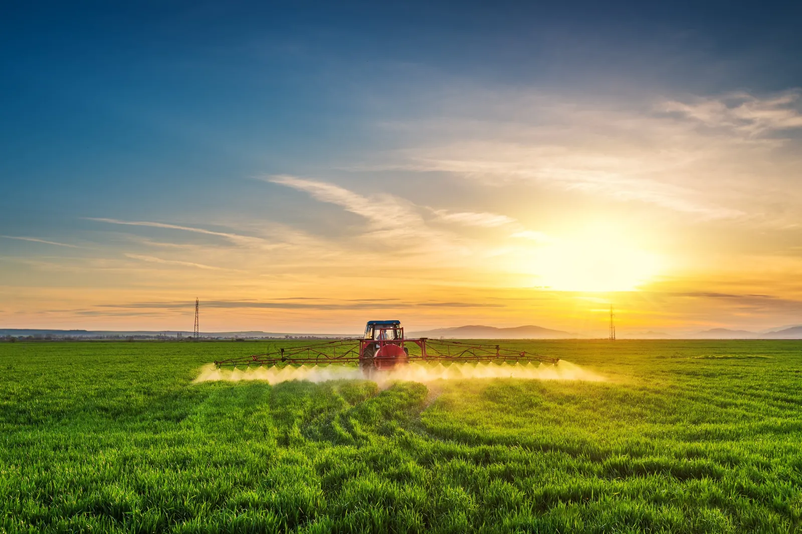 Tractor spraying a green field at sunset